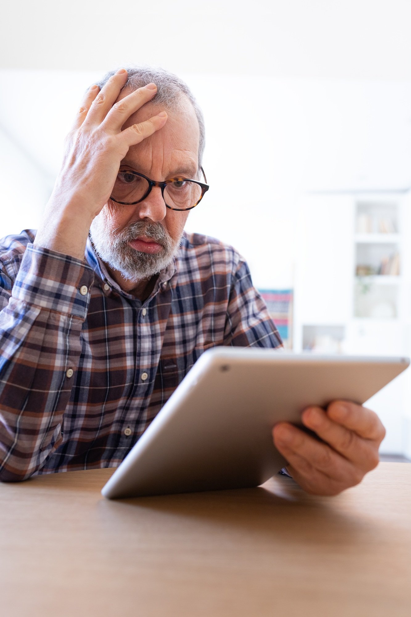 Stressed sen man having problems doing taxes online with digital tablet at home feeling overwhelmed.